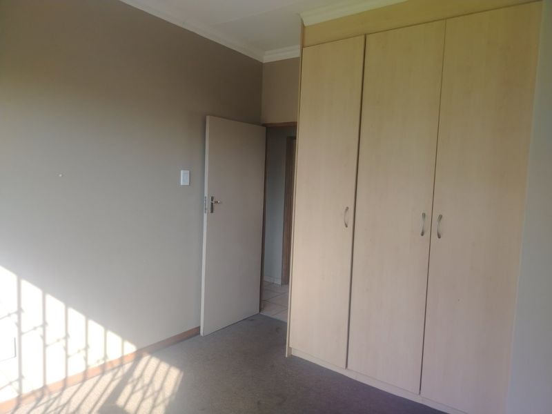 A clean, empty bedroom featuring neutral wall tones, carpeted flooring, and ample built-in cupboard storage space.