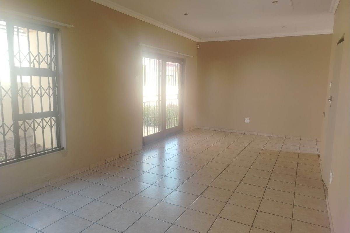 A spacious, empty living area featuring neutral tiled flooring, recessed lighting, and sliding glass doors with security gates leading to the exterior.