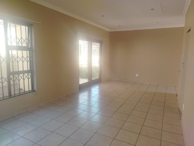 A spacious, empty living area featuring neutral tiled flooring, recessed lighting, and sliding glass doors with security gates leading to the exterior.