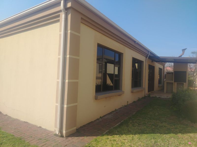 Rear exterior view of the house featuring a paved walkway, aluminium windows, and a covered patio area with a built-in braai.