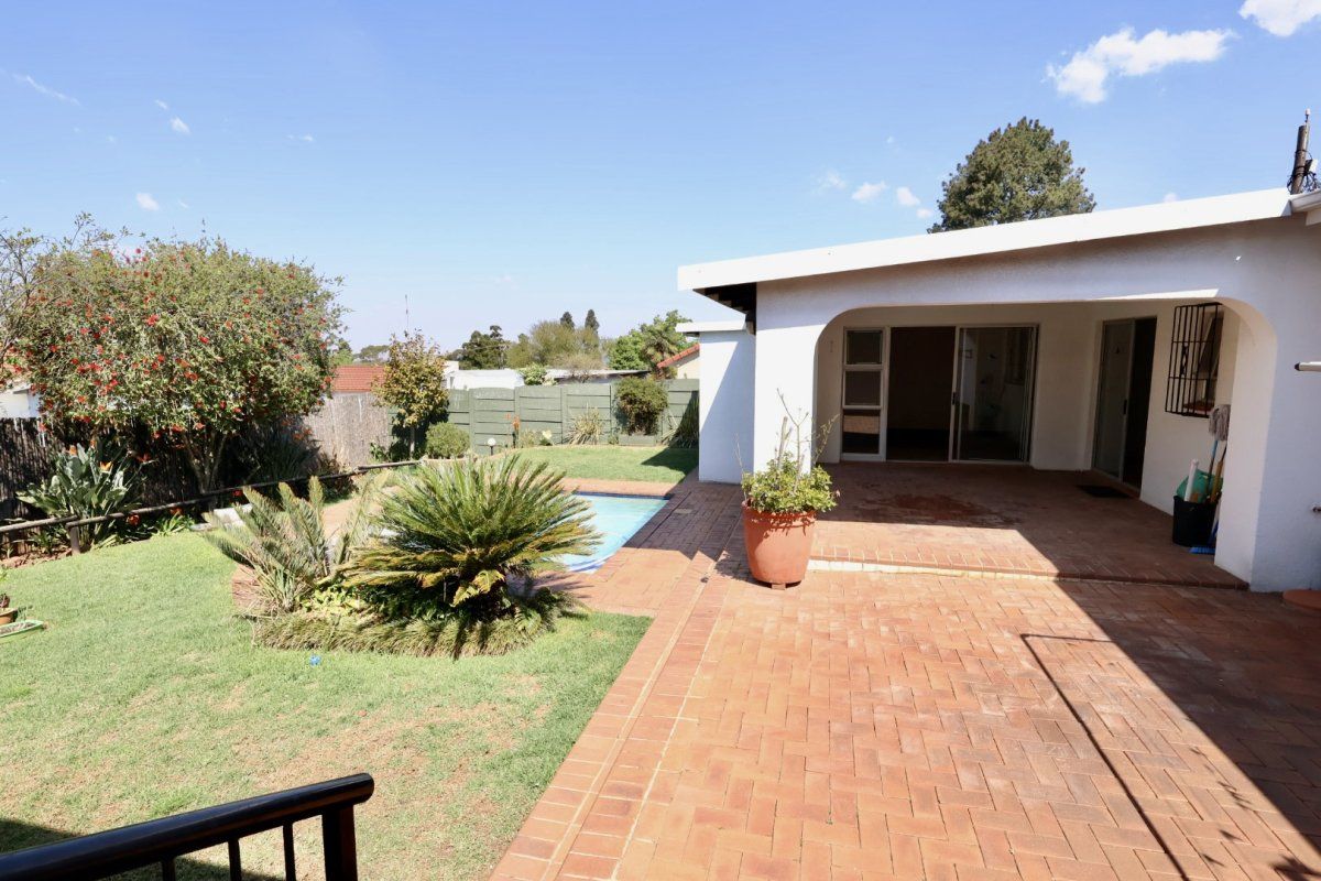 Rear view of the property featuring a covered brick-paved patio, a swimming pool, and a landscaped garden area.