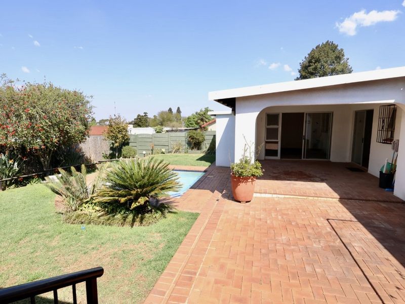 Rear view of the property featuring a covered brick-paved patio, a swimming pool, and a landscaped garden area.