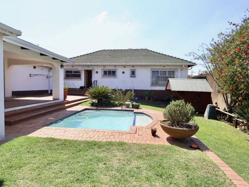 Rear view of the property featuring a swimming pool, covered patio area, and established garden with brick paving.