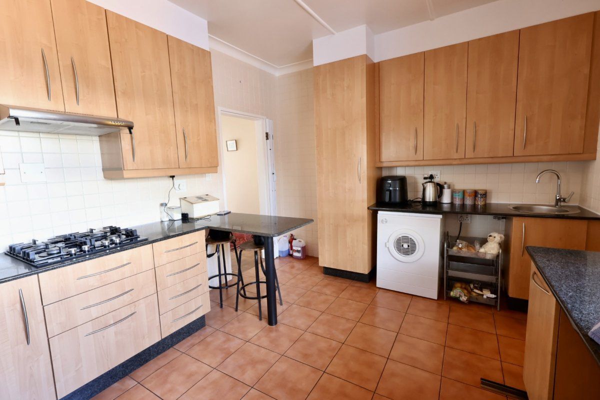 Functional kitchen featuring light wood cabinetry, dark countertops, gas hob with extractor, and tiled flooring, offering a practical layout for daily meal preparation.