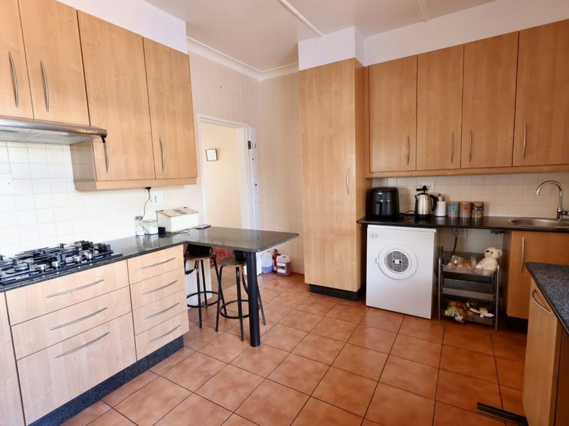 Functional kitchen featuring light wood cabinetry, dark countertops, gas hob with extractor, and tiled flooring, offering a practical layout for daily meal preparation.