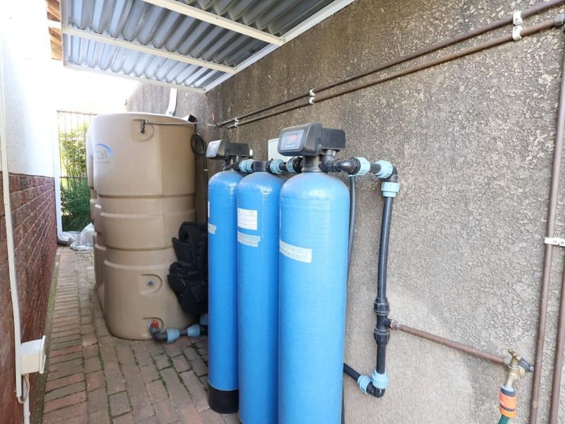 Utility area featuring a water storage tank and a multi-stage water filtration system installed against an exterior wall under a covered roof.