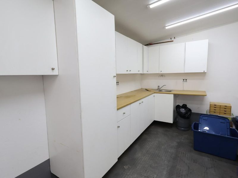 A functional scullery or utility area featuring white built-in cabinetry, a laminate countertop, and a stainless steel sink.
