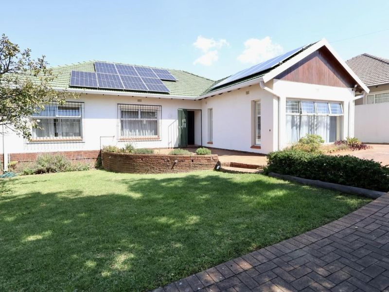 Rear view of the house featuring a paved patio, landscaped garden, and roof-mounted solar panels.