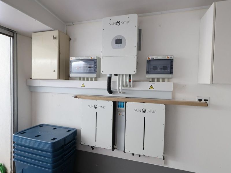 A clean utility area featuring a modern Sunsynk solar inverter and battery storage system installation.