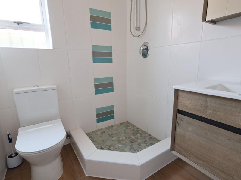 A clean, modern bathroom featuring a corner shower with pebble-style floor tiling, a wall-mounted vanity, and a white toilet.