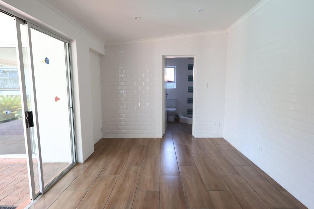 A bright, empty living area featuring wood-look tile flooring, white subway tile feature walls, and a sliding glass door leading to an outdoor patio.