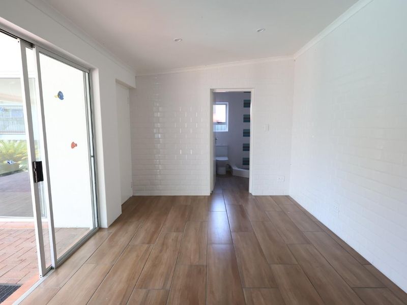 A bright, empty living area featuring wood-look tile flooring, white subway tile feature walls, and a sliding glass door leading to an outdoor patio.
