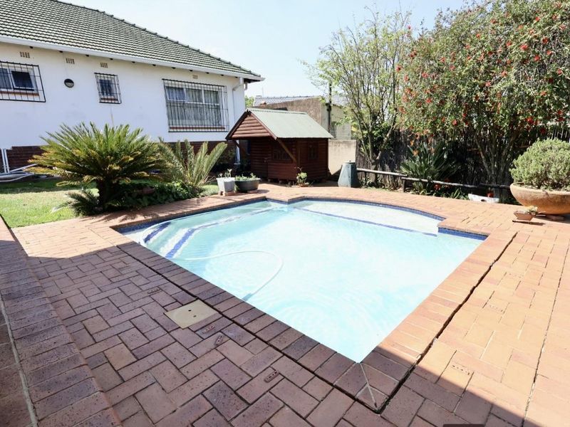 A well-maintained outdoor pool area featuring brick paving, a clear swimming pool, and a landscaped garden setting adjacent to the main house.