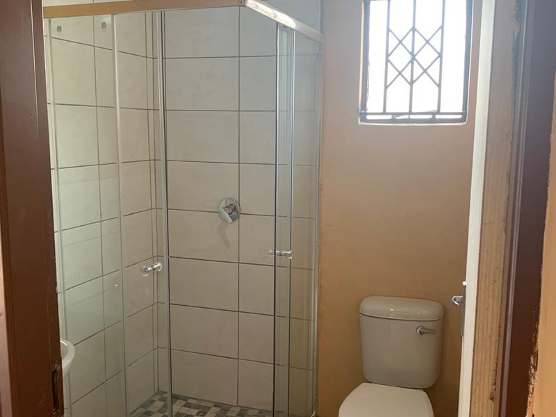 A compact bathroom featuring a glass shower enclosure, a standard toilet, and tiled finishes, requiring minor cosmetic updates to improve its overall presentation.