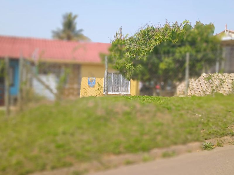 A street-level view of a residential property featuring a metal roof, stone retaining wall, and perimeter fencing.