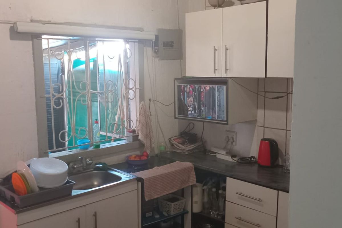 A compact kitchen featuring built-in cabinetry, laminate countertops, and a stainless steel sink, with security bars installed on the window.