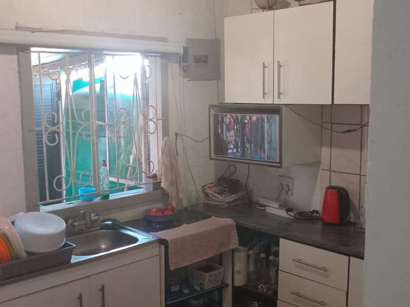 A compact kitchen featuring built-in cabinetry, laminate countertops, and a stainless steel sink, with security bars installed on the window.