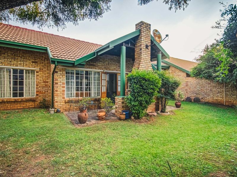 Rear view of a brick house featuring a covered patio area, established garden, and a tiled roof.