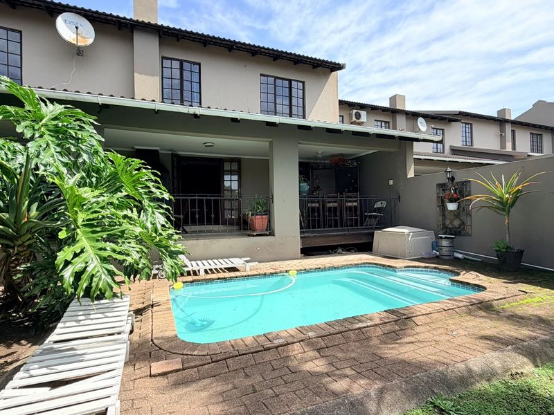 Rear exterior view of the townhouse featuring a private swimming pool, covered patio area, and brick-paved garden space.