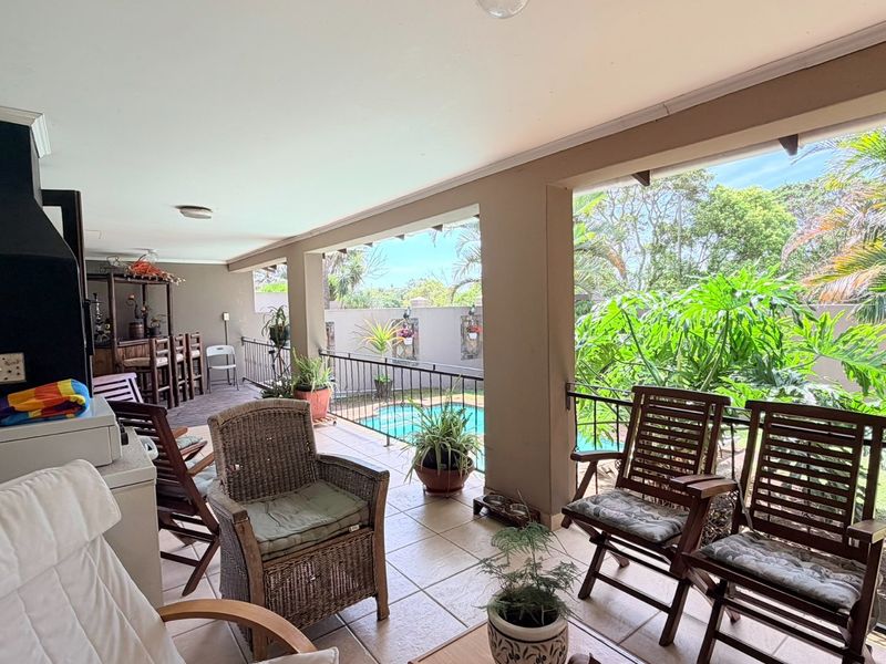 Spacious covered patio featuring a built-in braai, tiled flooring, and wrought iron balustrades, overlooking the garden and swimming pool area.