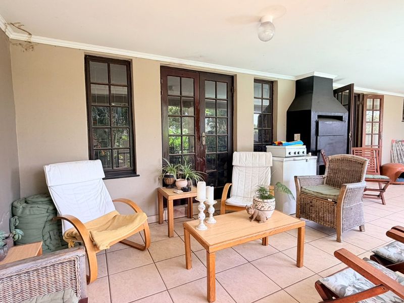 Covered patio area featuring tiled flooring, a built-in braai, and access to the interior via timber-framed french doors.