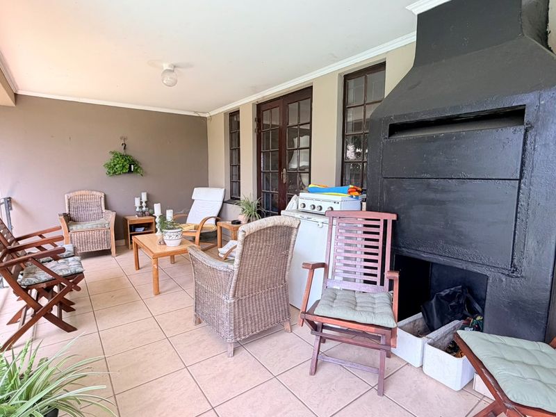 Covered patio area featuring tiled flooring and a large built-in braai, providing a functional outdoor entertainment space.