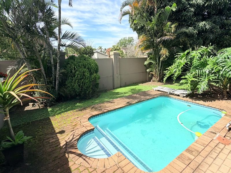 Private backyard area featuring a swimming pool, brick paved surround, and established garden landscaping enclosed by a solid boundary wall.