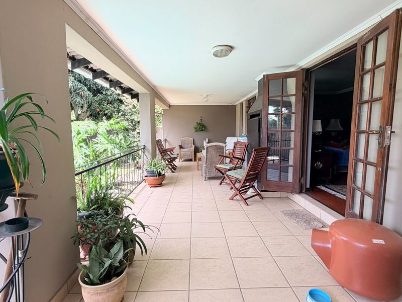 A spacious covered patio featuring tiled flooring, a built-in braai, and direct access to the interior through classic wooden french doors.