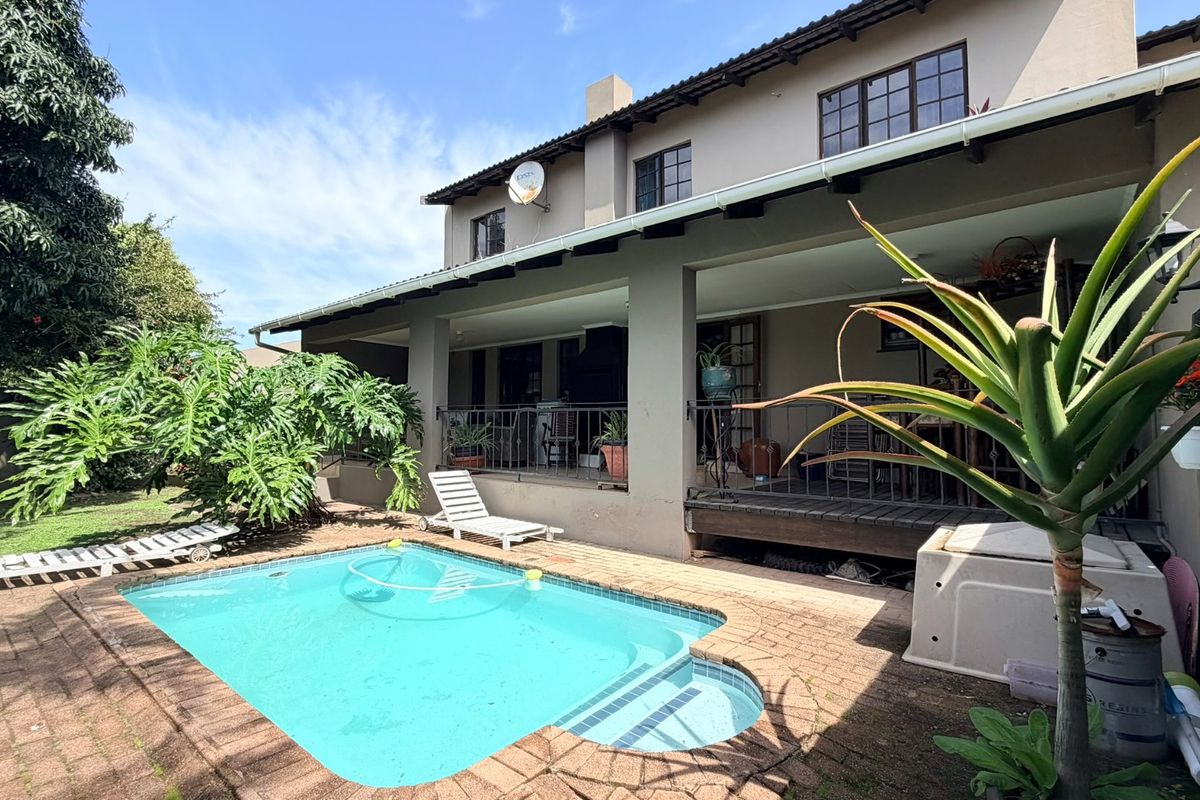 Rear view of the townhouse featuring a covered patio area overlooking a private swimming pool and landscaped garden space.