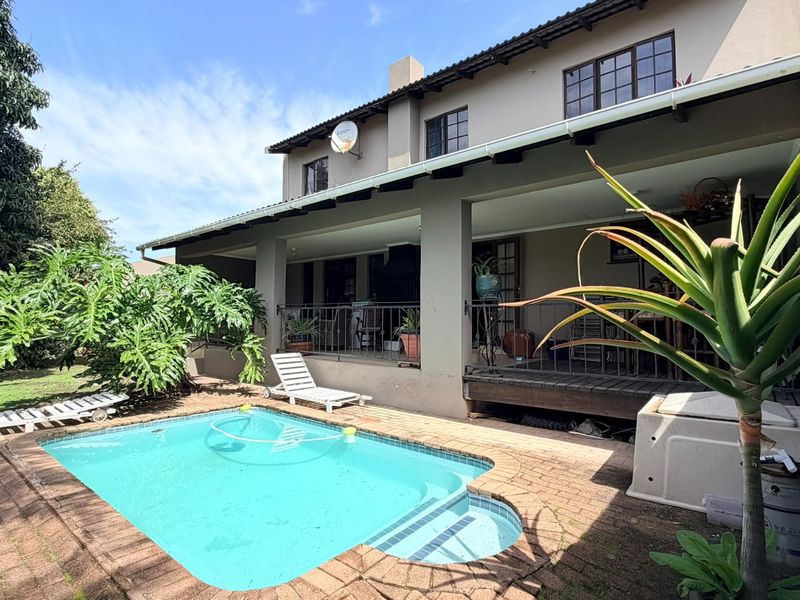 Rear view of the townhouse featuring a covered patio area overlooking a private swimming pool and landscaped garden space.
