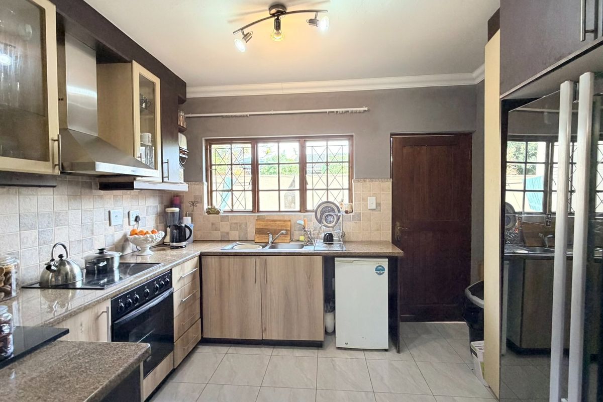 Functional kitchen featuring wood-finish cabinetry, granite countertops, built-in oven with hob, extractor fan, and tiled flooring with a window overlooking the exterior.