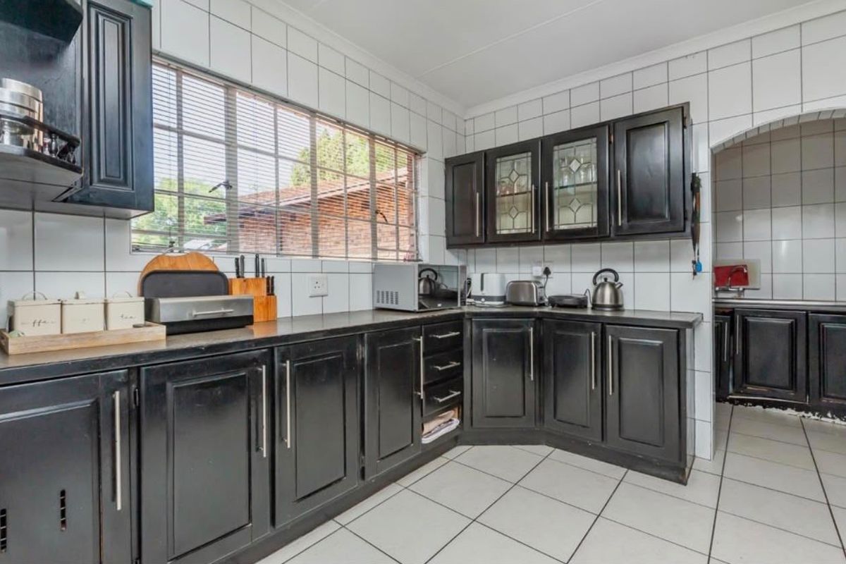 A functional kitchen featuring dark cabinetry, white tiled backsplash, and tiled flooring, with an adjacent scullery area visible through the archway.