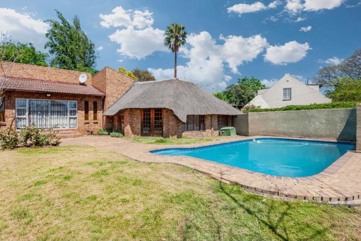 Rear exterior view featuring a swimming pool, brick-paved patio area, and a unique thatched-roof structure set against a brick house facade.