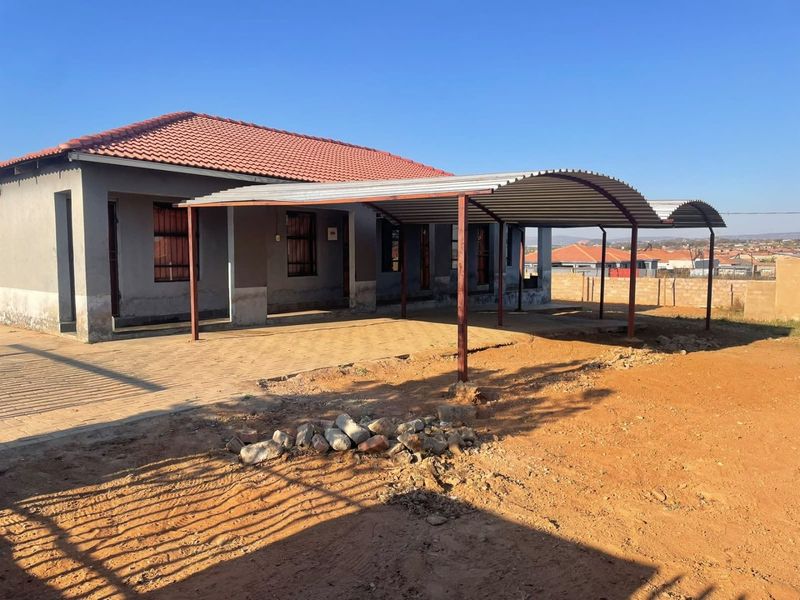 Front exterior view of a commercial property featuring a large corrugated metal carport, paved driveway, and tiled roof with security bars on windows.