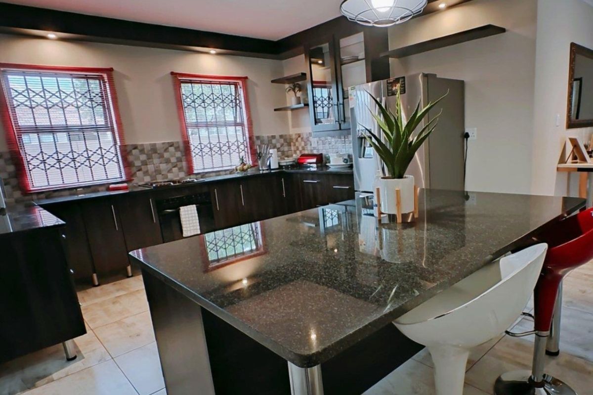 Modern kitchen featuring dark cabinetry, granite countertops, a central island, and tiled flooring with ample natural light from windows with security bars.