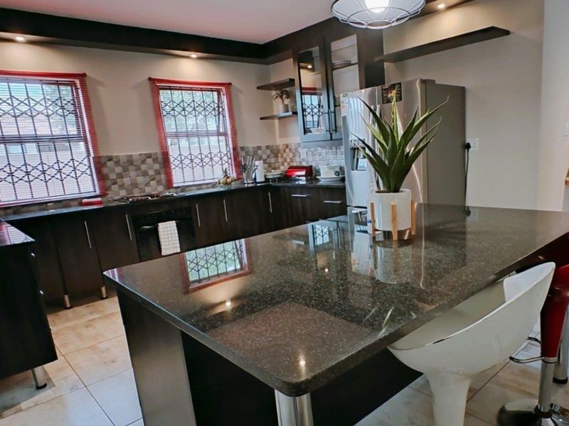 Modern kitchen featuring dark cabinetry, granite countertops, a central island, and tiled flooring with ample natural light from windows with security bars.