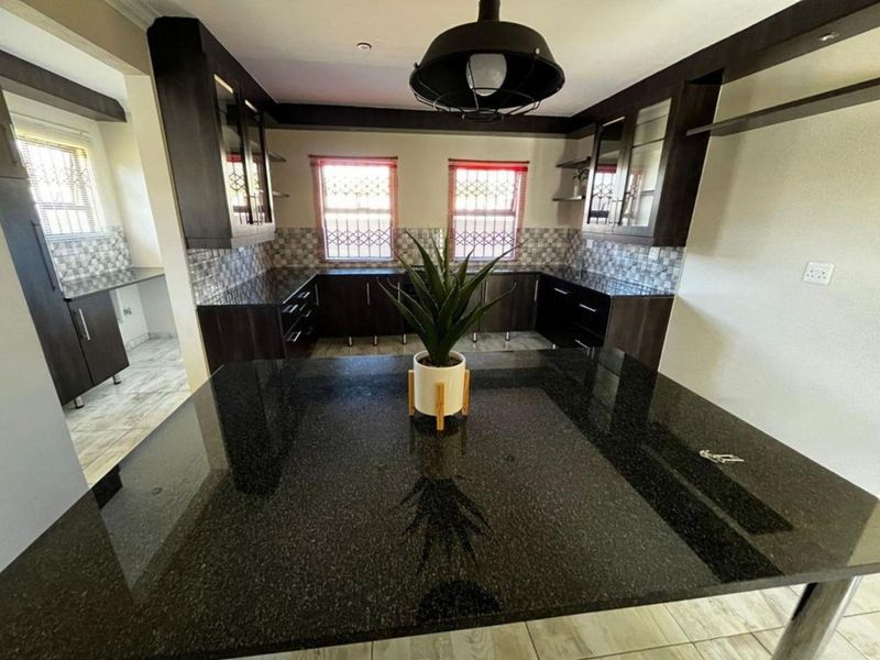 Modern kitchen featuring dark cabinetry, granite countertops, a central island, and tiled backsplash with natural light from dual windows.