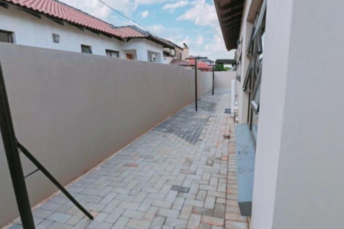 A side exterior walkway featuring paved flooring and a high boundary wall, providing a clean and functional outdoor utility space.