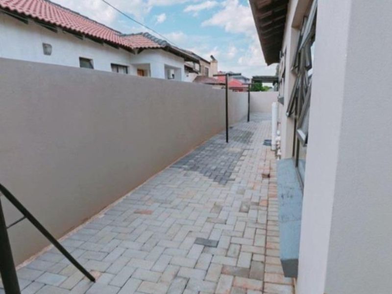 A side exterior walkway featuring paved flooring and a high boundary wall, providing a clean and functional outdoor utility space.