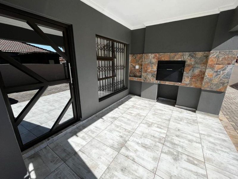 Covered patio area featuring a built-in braai, modern tiled flooring, and secure access points, ideal for outdoor entertaining.