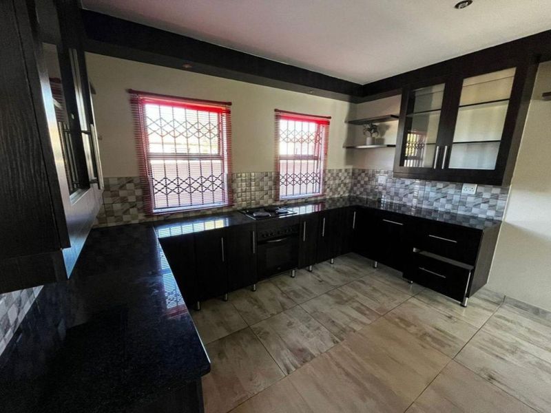 Modern kitchen featuring dark cabinetry, granite countertops, built-in oven and hob, tiled backsplash, and large floor tiles.