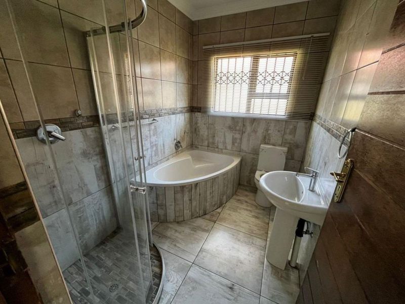 A functional bathroom featuring a corner bathtub, separate glass shower enclosure, pedestal basin, and toilet with neutral wall and floor tiling.