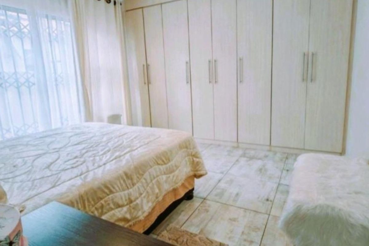 A well-maintained bedroom featuring extensive built-in cupboards, light-toned tiled flooring, and large windows with security gates for added safety.