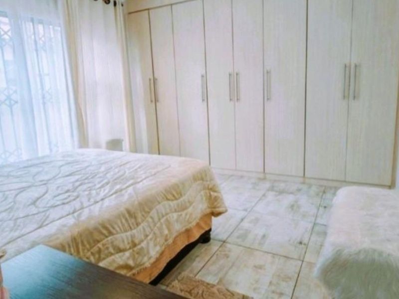 A well-maintained bedroom featuring extensive built-in cupboards, light-toned tiled flooring, and large windows with security gates for added safety.
