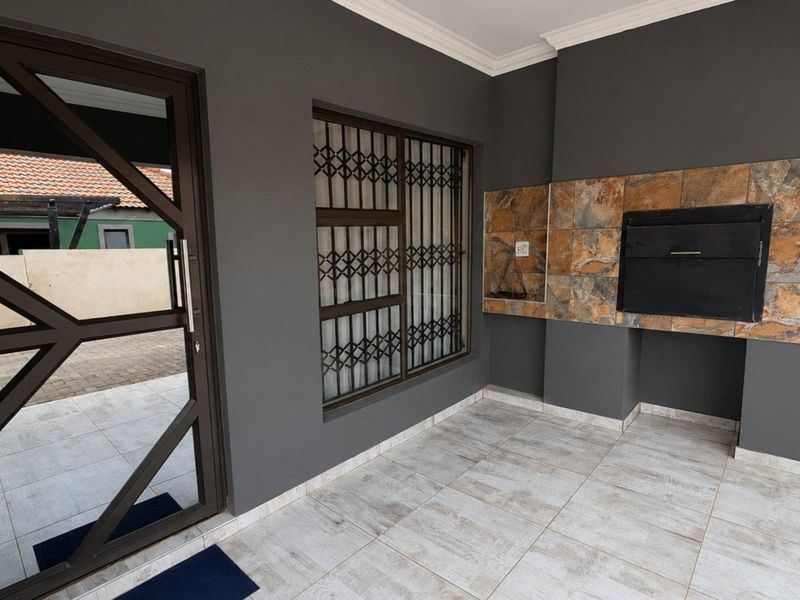 A covered patio area featuring tiled flooring, a built-in braai with stone cladding, and secure access via a metal security gate.
