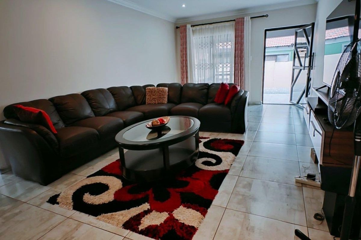 A well-maintained living room featuring neutral tiled flooring, recessed lighting, and direct access to an outdoor area through a sliding door.