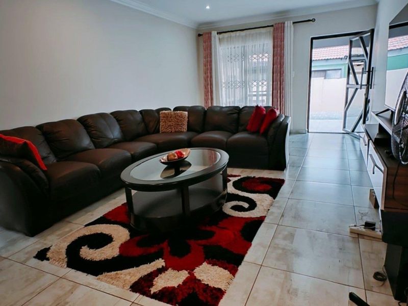 A well-maintained living room featuring neutral tiled flooring, recessed lighting, and direct access to an outdoor area through a sliding door.