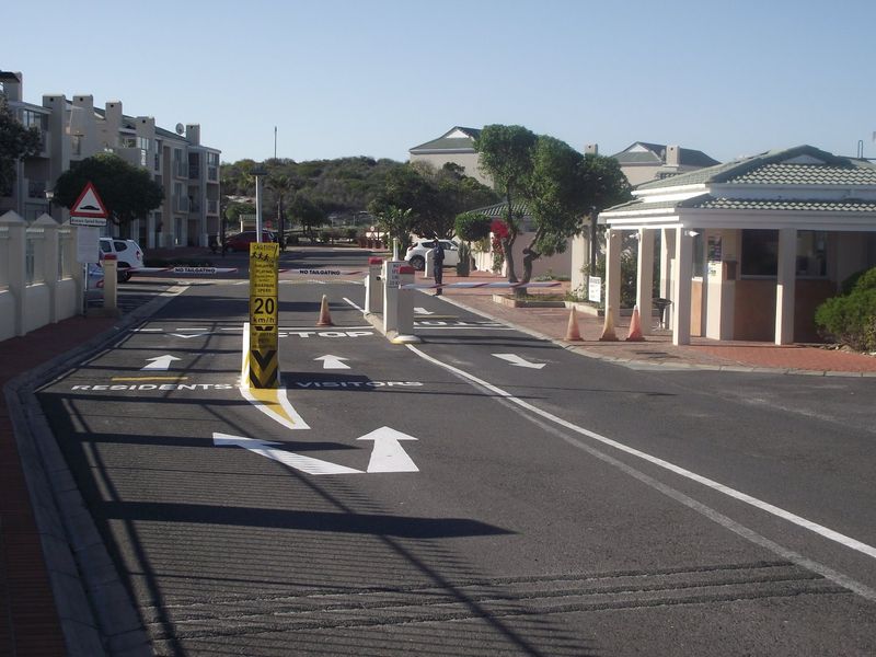 The secure entrance to the apartment complex features a guarded gatehouse, boom barriers, and clearly marked residential and visitor access lanes.