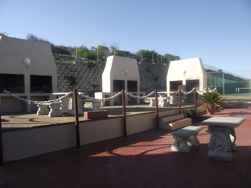Outdoor communal entertainment area featuring multiple built-in braai stations, concrete seating, and brick paving set against a retaining wall.