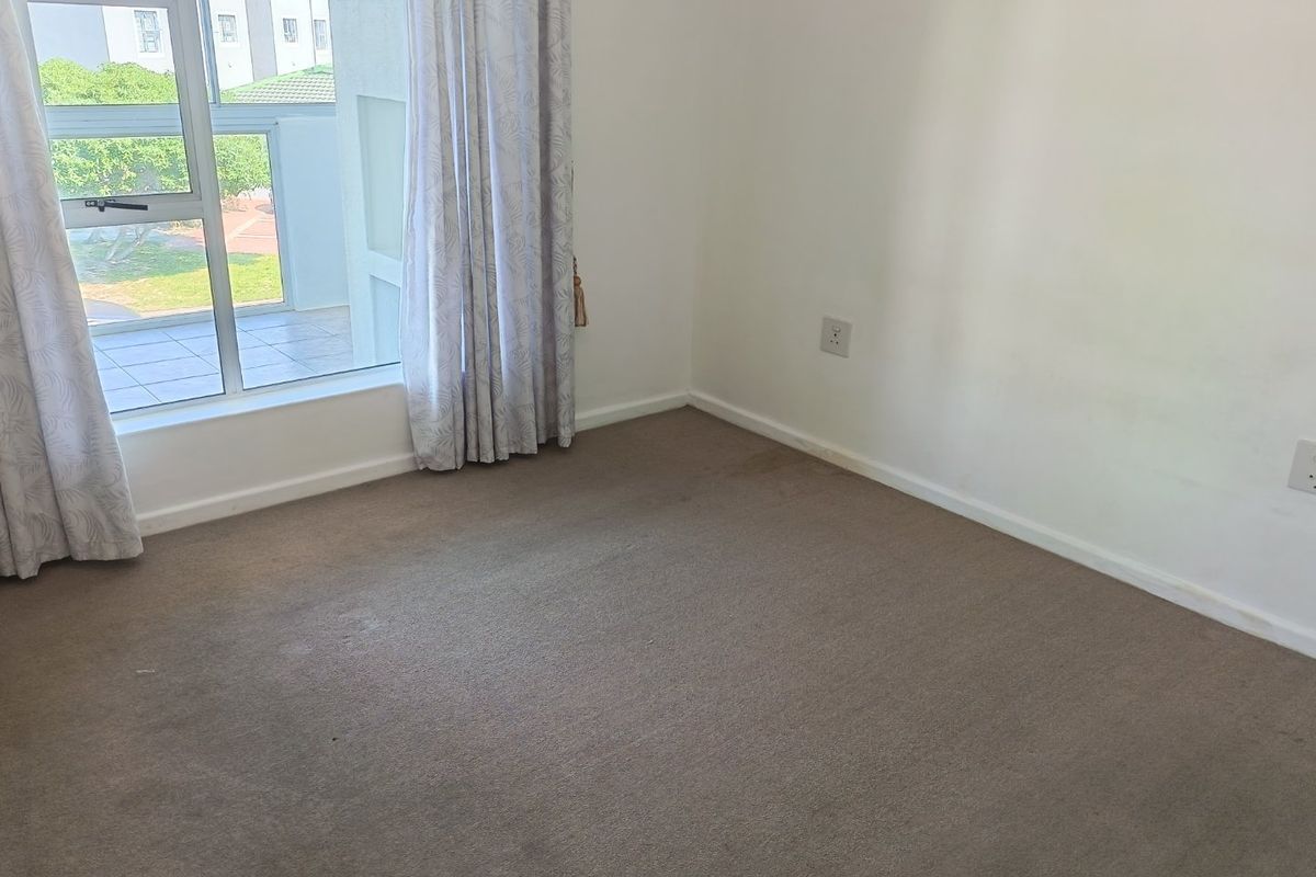 An empty bedroom featuring carpeted flooring, neutral walls, and a sliding window providing access to an adjacent balcony area.
